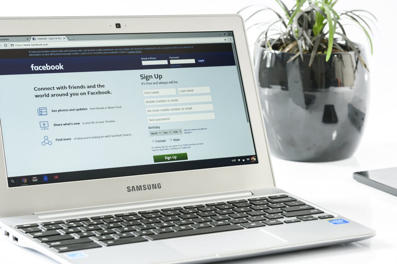 Open Samsung laptop showing Facebook sign-up page next to a potted plant. Ideal for technology themes.