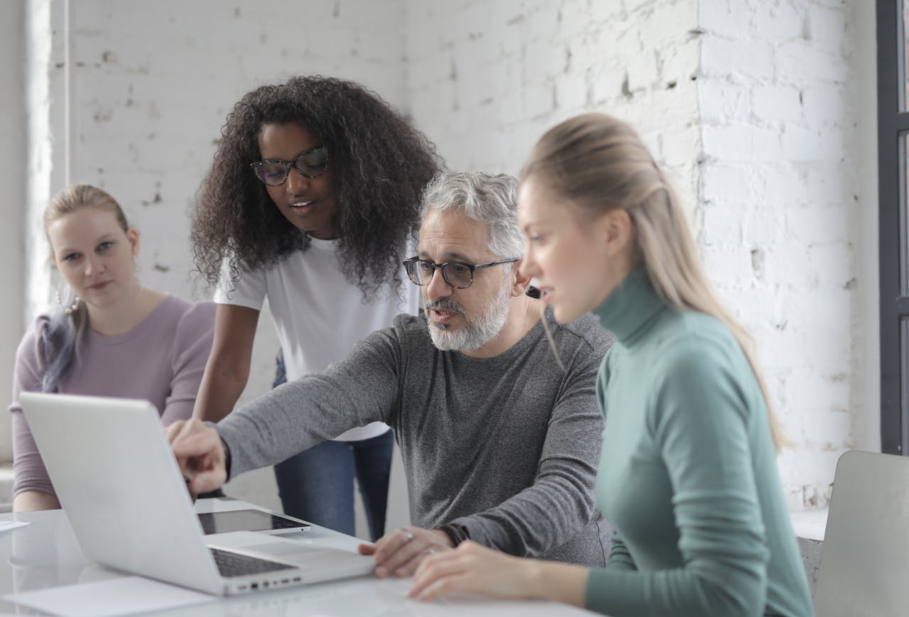 A group of colleagues discussing a project on a laptop in a bright office setting.