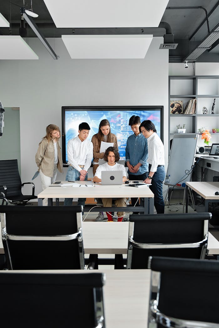 A group of colleagues collaborating around a laptop in a contemporary office environment.